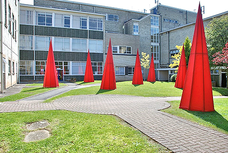 Seven red cone-shaped objects rising from the courtyard grass