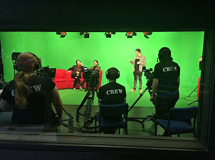 View of TV studio with presenter and technicians and a green screen behind