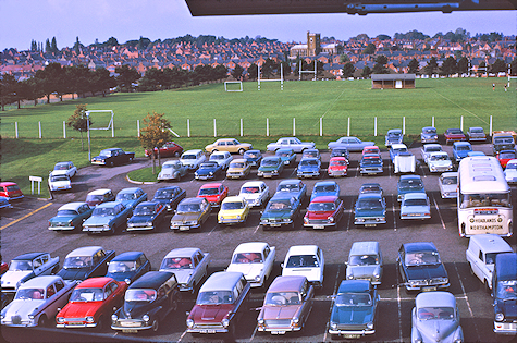 Vehicles parked in the rear car park, with a grass field beyond a fence