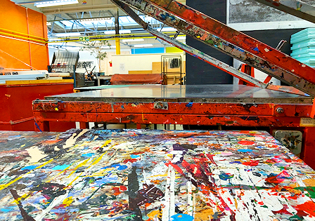 Photo of a printing press with lots of coloured ink lines and spatters on a table